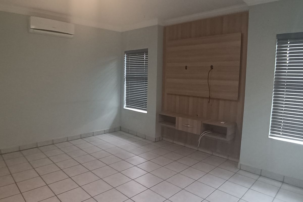 An empty living room featuring tiled flooring, a built-in media console, air conditioning, and venetian blinds.