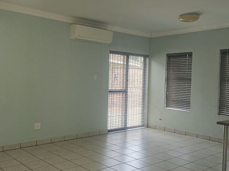 A spacious, empty living area featuring tiled flooring, crown molding, an air conditioning unit, and sliding glass doors with venetian blinds.