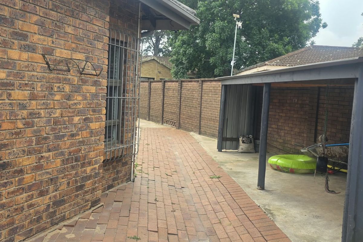 A side exterior view of the property featuring a brick facade, paved walkway, and a covered carport area with perimeter brick walling.