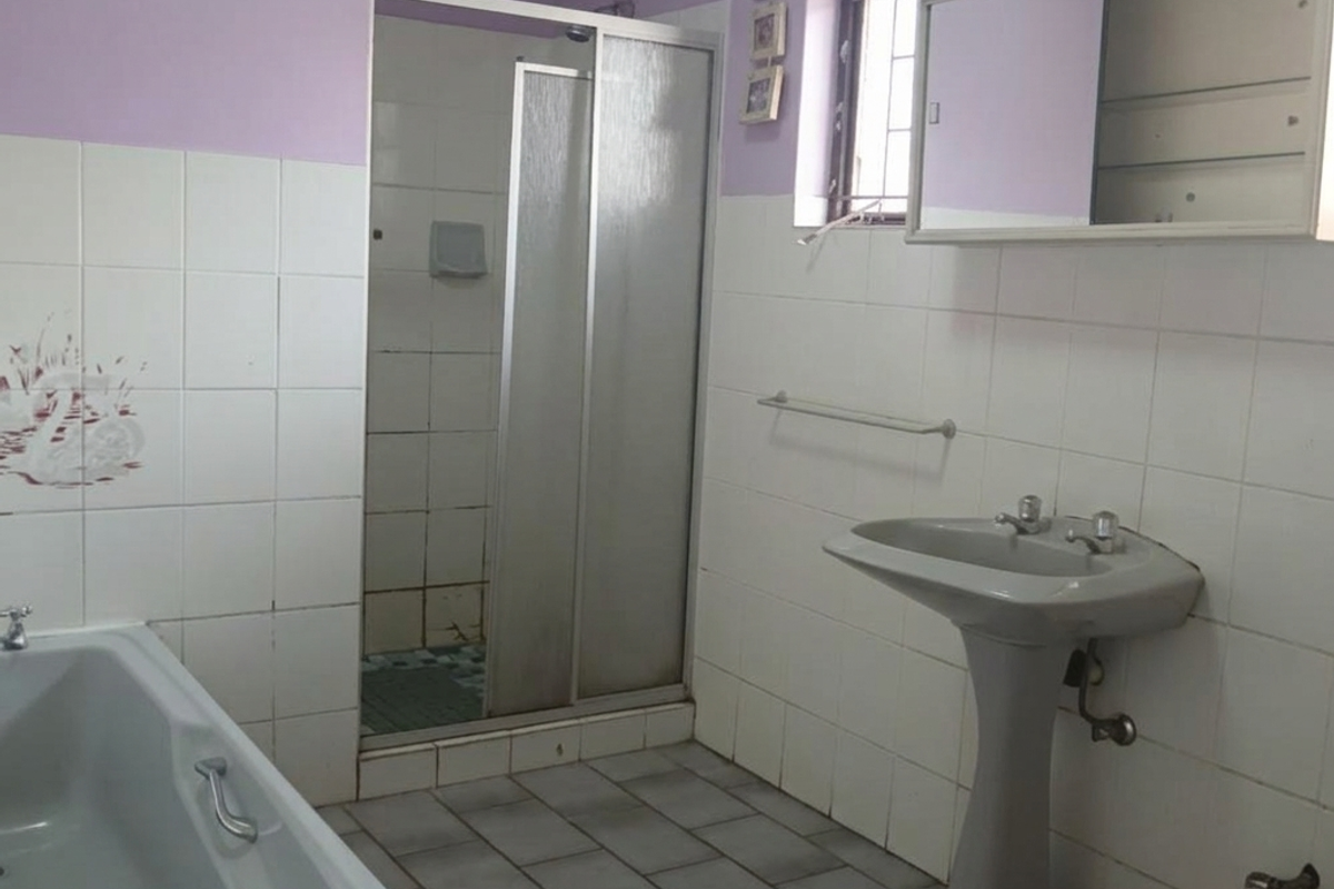 A functional bathroom featuring a pedestal basin, shower enclosure, and bathtub with tiled finishes, offering potential for modernization and cosmetic updates.