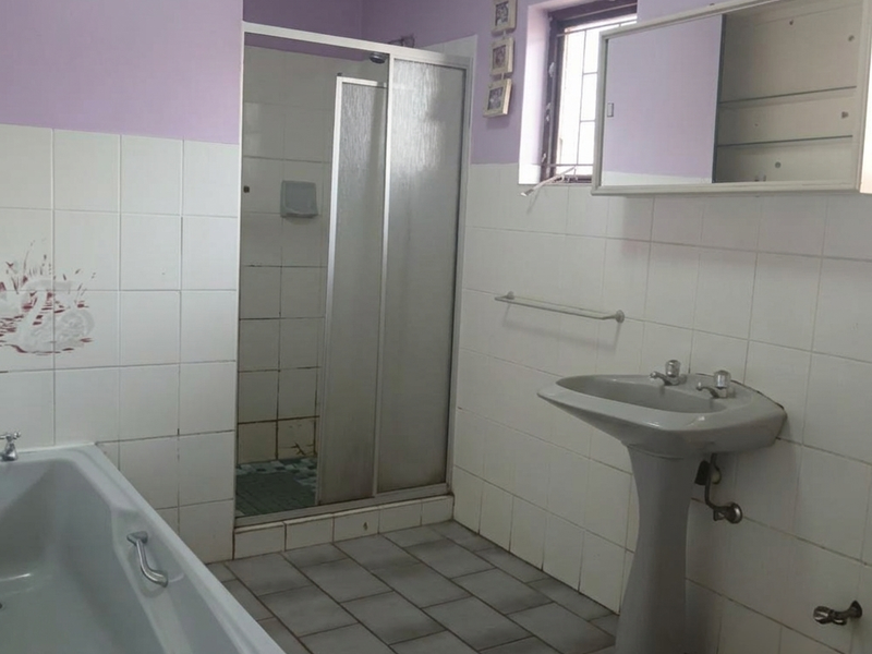 A functional bathroom featuring a pedestal basin, shower enclosure, and bathtub with tiled finishes, offering potential for modernization and cosmetic updates.