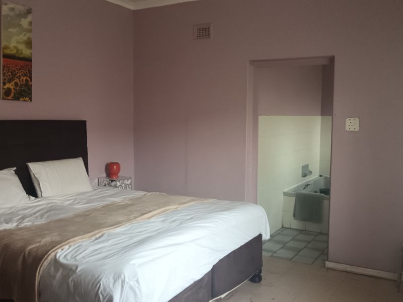 Bedroom featuring an en-suite bathroom access, neutral wall tones, and tiled flooring. The space offers a functional layout ready for cosmetic updates.