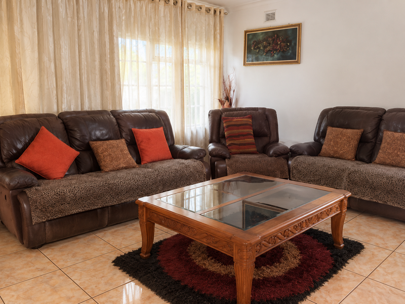 A comfortable living room featuring neutral tiled flooring and large windows dressed with curtains, providing a bright and functional space for relaxation.