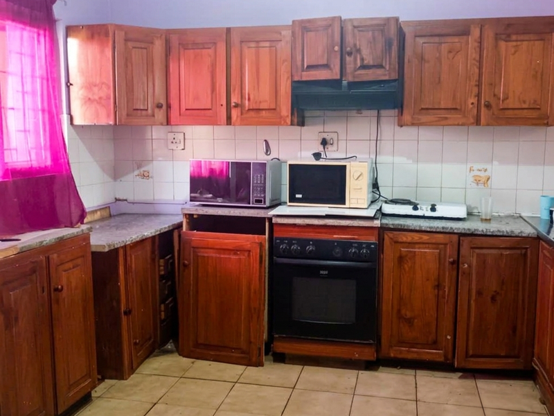 A dated kitchen featuring wooden cabinetry, a built-in oven with extractor fan, tiled backsplash, and tiled flooring in need of maintenance.