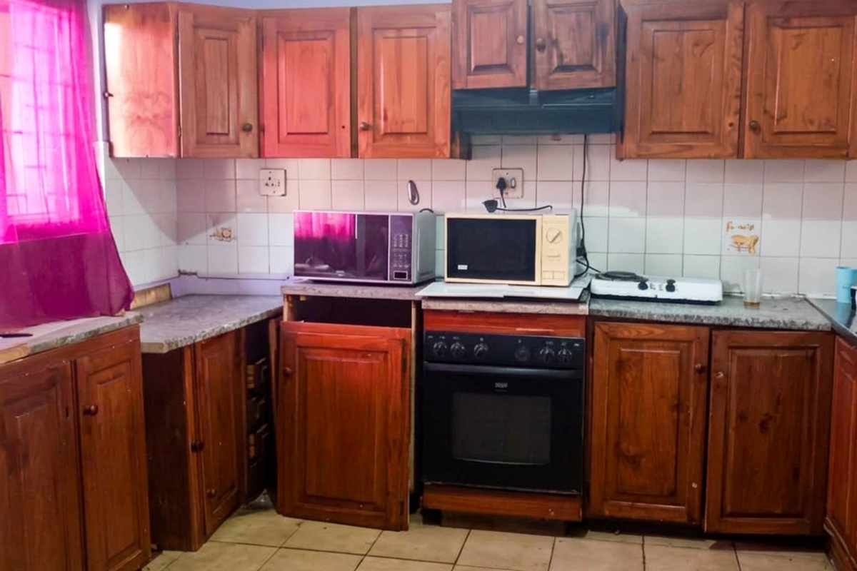A dated kitchen featuring wooden cabinetry, a built-in oven with extractor fan, tiled backsplash, and tiled flooring in need of maintenance.