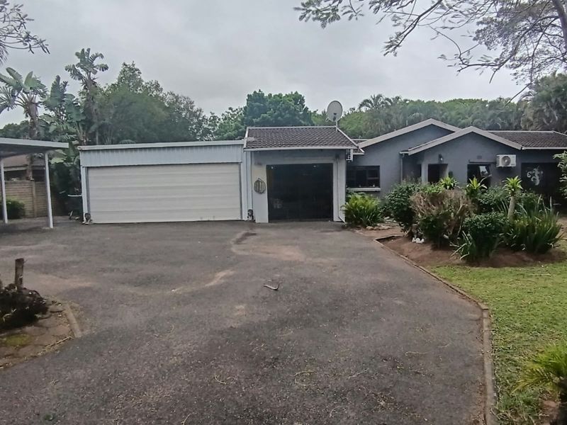 Front view of a residential property featuring a spacious asphalt driveway, a double garage, and an attached carport with established garden landscaping.
