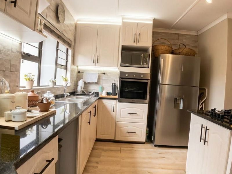 Modern kitchen featuring light wood-finish cabinetry, granite countertops, integrated appliances including an oven and microwave, and durable laminate flooring.