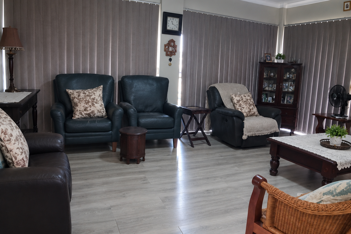 A spacious living room featuring modern light-toned laminate flooring, ceiling fan, and full-length vertical blinds covering the windows.