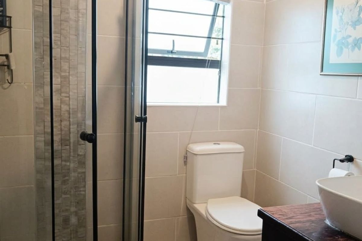 A modern bathroom featuring a glass-enclosed shower with decorative tiling, a white toilet, and a vanity basin with a wooden countertop.