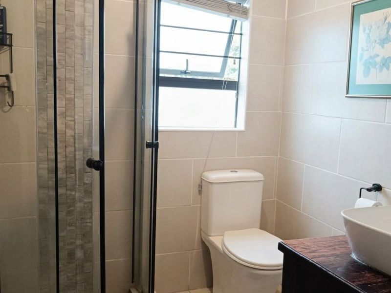 A modern bathroom featuring a glass-enclosed shower with decorative tiling, a white toilet, and a vanity basin with a wooden countertop.