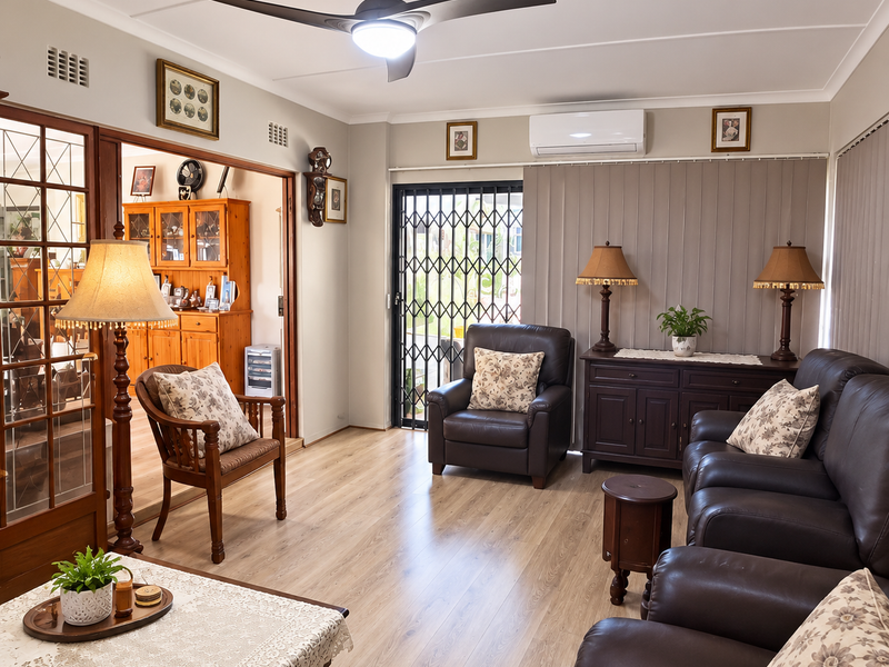 A well-maintained living room featuring laminate flooring, a ceiling fan, and a split-system air conditioner, with direct access to an outdoor area via security gate.
