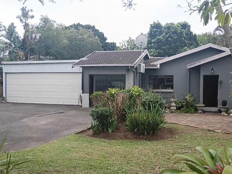 Front view of a single-story house featuring a paved driveway, attached garage, and established garden area.