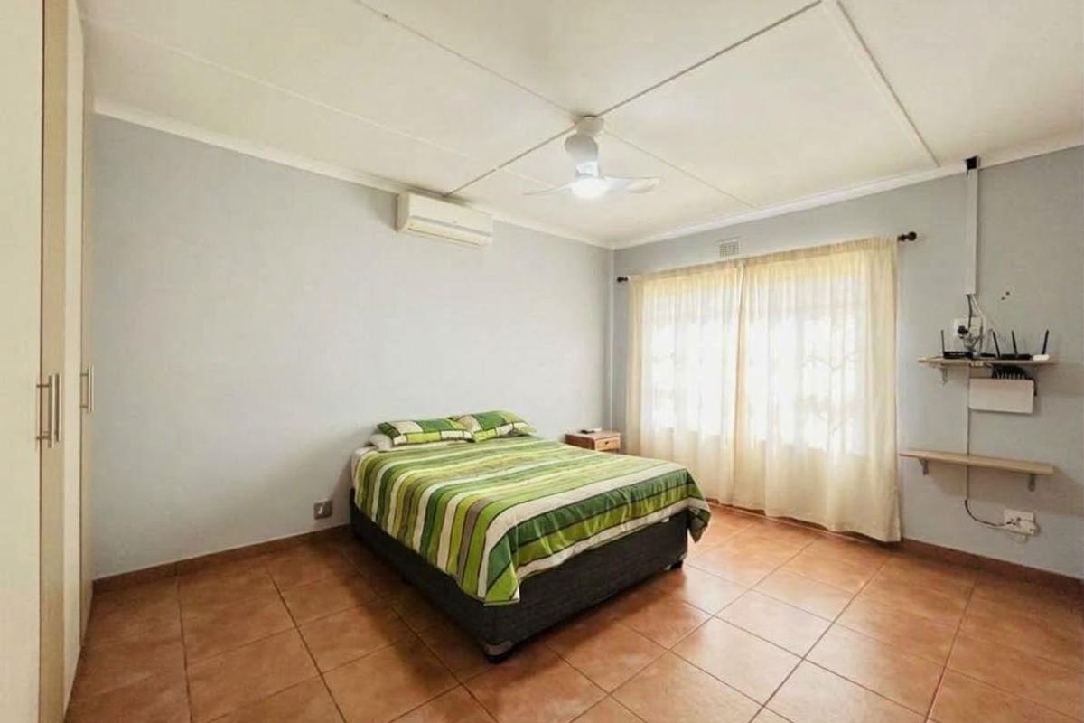 A functional bedroom featuring tiled flooring, built-in cupboards, a ceiling fan, and a wall-mounted air conditioning unit.