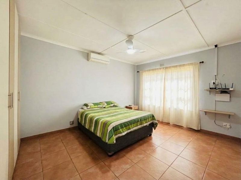 A functional bedroom featuring tiled flooring, built-in cupboards, a ceiling fan, and a wall-mounted air conditioning unit.