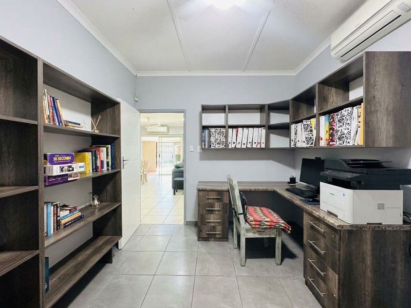 A functional home office featuring extensive built-in cabinetry, shelving, tiled flooring, and a wall-mounted air conditioning unit.