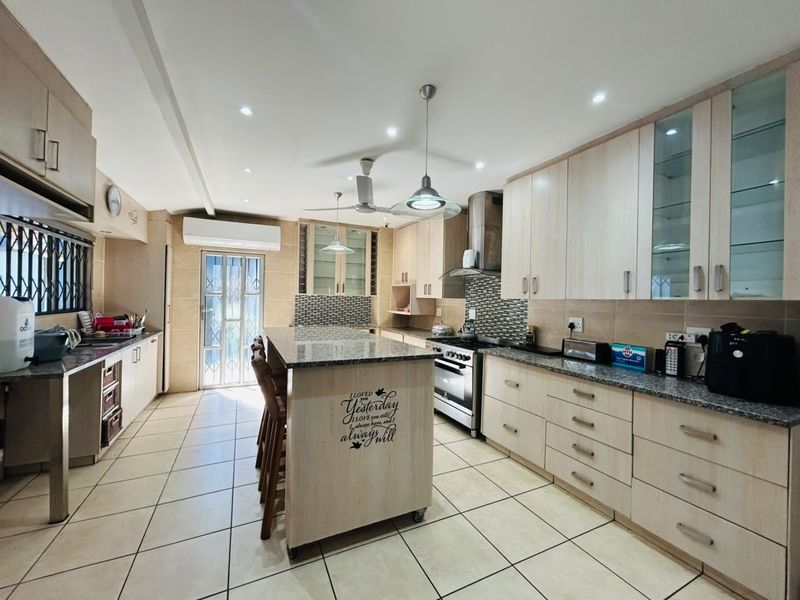 Spacious kitchen featuring light wood cabinetry, granite countertops, a central island, tiled flooring, and modern built-in appliances.