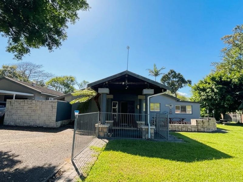 Front view of a single-story house featuring a covered porch, stone-clad accents, a paved driveway, and an attached carport set within a spacious garden.