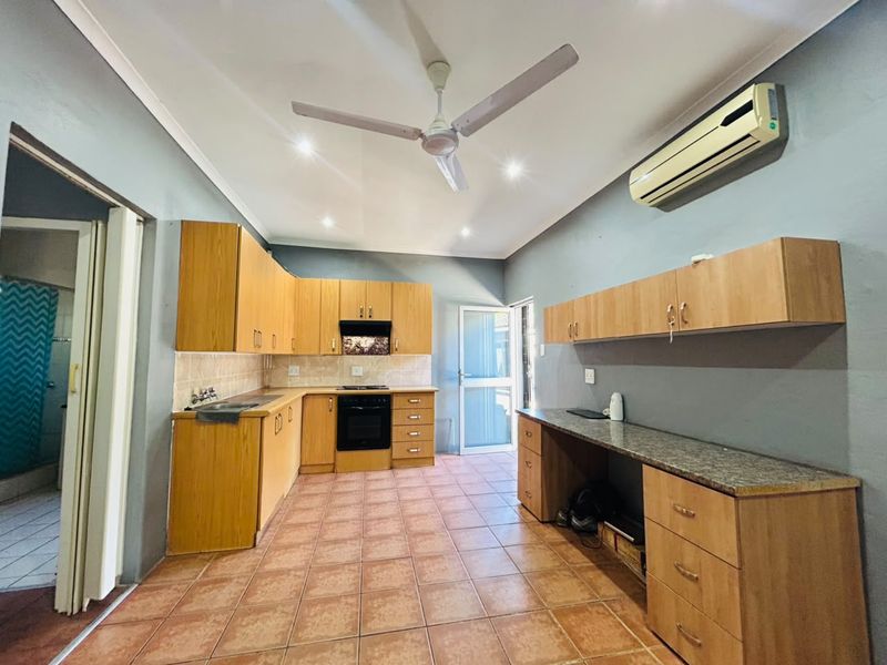 Spacious kitchen featuring extensive wooden cabinetry, granite countertops, built-in oven, extractor fan, and tiled flooring, offering a functional layout with ample storage space.