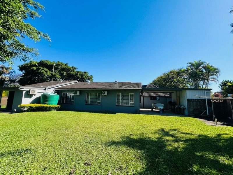 Rear view of the property featuring a spacious lawn, tiled roof, security bars on windows, and an attached carport area.
