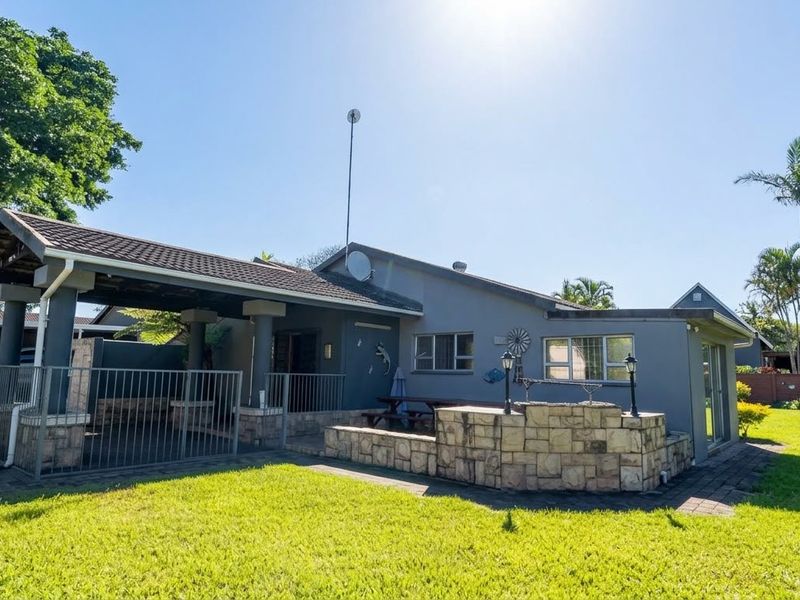 Rear view of the house featuring a covered patio area, stone-clad built-in braai, and a well-maintained garden.
