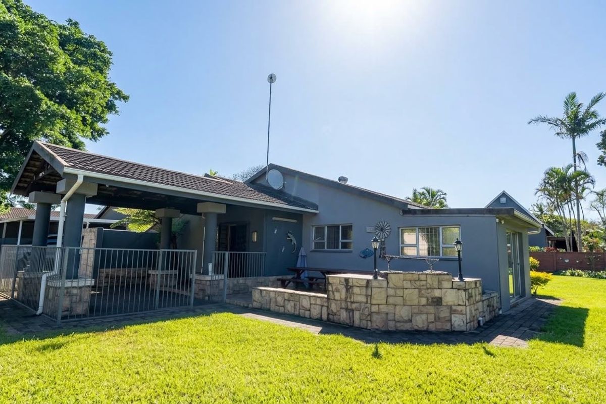 Rear view of the house featuring a covered patio area, stone-clad built-in braai, and a well-maintained garden.