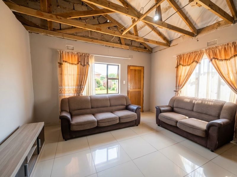Living room featuring tiled flooring, exposed timber roof trusses, and natural light through aluminium windows.