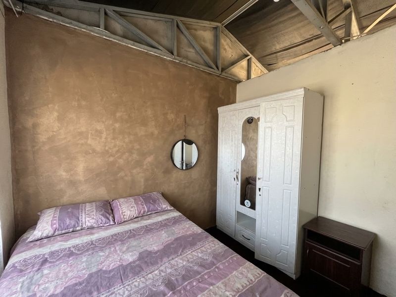 A bedroom featuring a textured feature wall and exposed steel roof trusses, offering a rustic industrial aesthetic with potential for modern refinement.