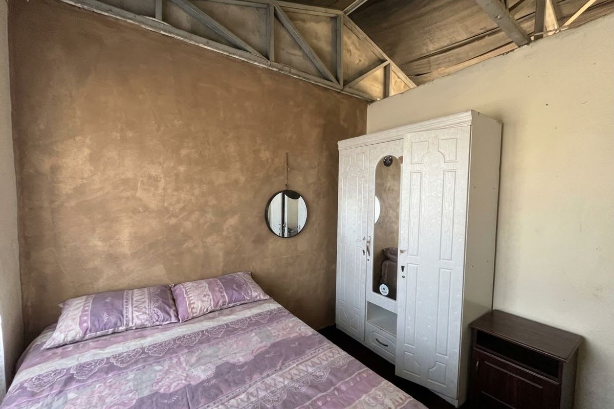 A bedroom featuring a textured feature wall and exposed steel roof trusses, offering a rustic industrial aesthetic with potential for modern refinement.