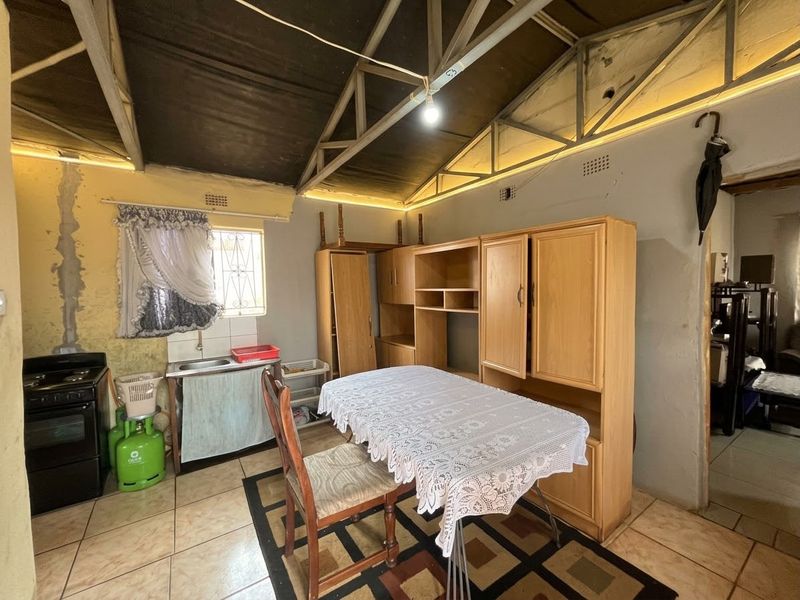 A rustic kitchen area featuring exposed roof trusses, tiled flooring, and a basic sink setup, requiring significant renovation and cosmetic updates.