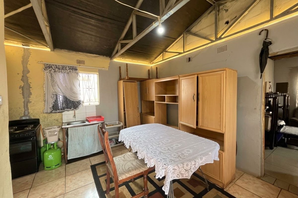 A rustic kitchen area featuring exposed roof trusses, tiled flooring, and a basic sink setup, requiring significant renovation and cosmetic updates.