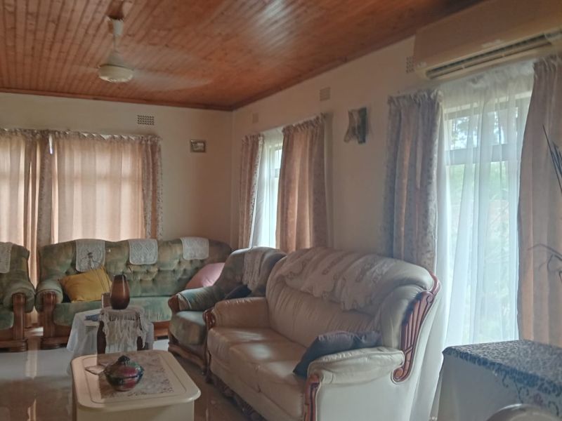 A spacious living room featuring a warm timber tongue and groove ceiling, tiled flooring, and a wall-mounted split system air conditioner.