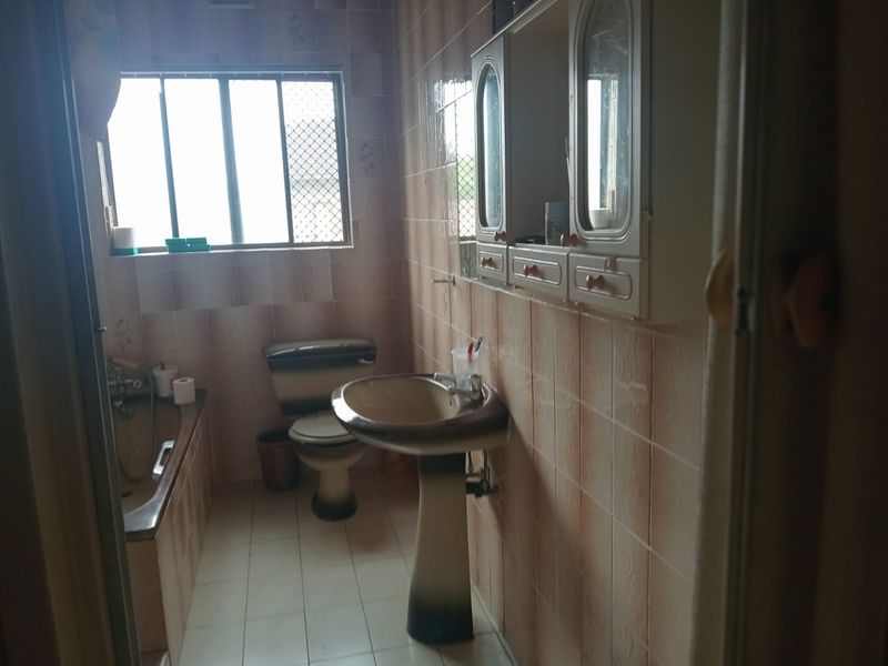 A dated bathroom featuring a pedestal basin, built-in bathtub, toilet, and wall-mounted cabinetry with full-height wall tiling.