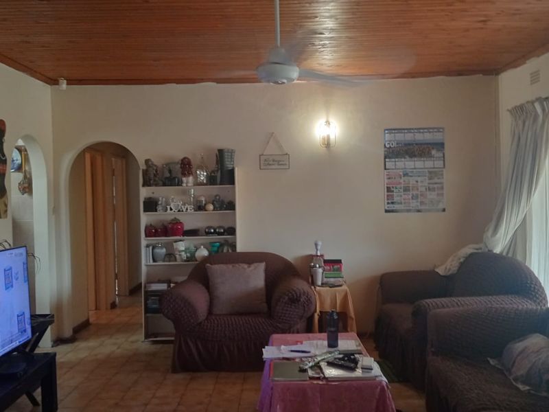 A living room featuring a timber-clad ceiling, ceiling fan, tiled flooring, and an arched doorway leading to the hallway.