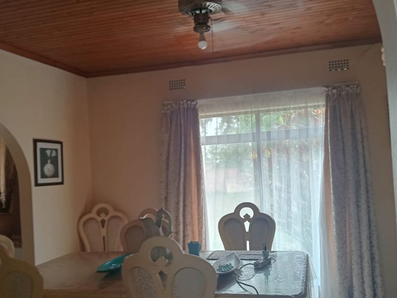 A dining room featuring a warm timber ceiling, a ceiling fan, and a large window that allows for natural light.