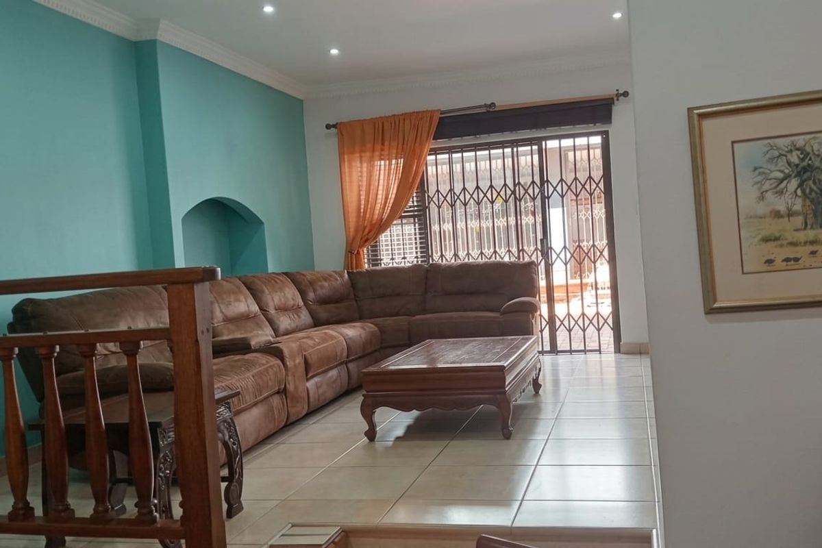A spacious living room featuring tiled flooring, recessed ceiling lighting, and a sliding door with security gate leading to the outdoor area.