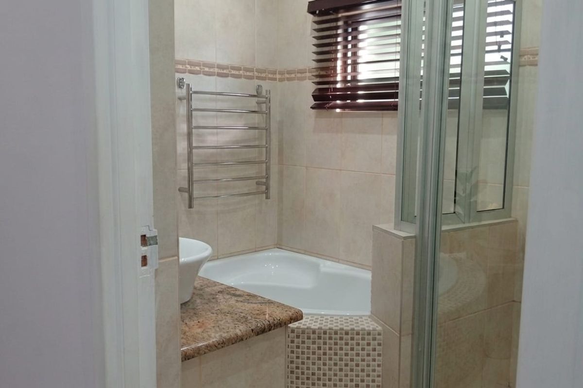 A compact bathroom featuring a corner bathtub, granite vanity top, vessel sink, and a wall-mounted heated towel rail.