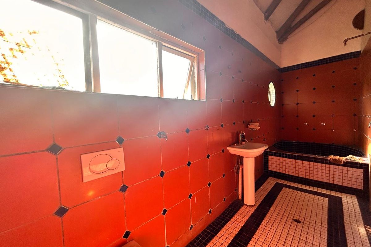 A dated bathroom featuring terracotta-style wall tiles, a pedestal basin, and a built-in bathtub with contrasting black and white floor tiling.