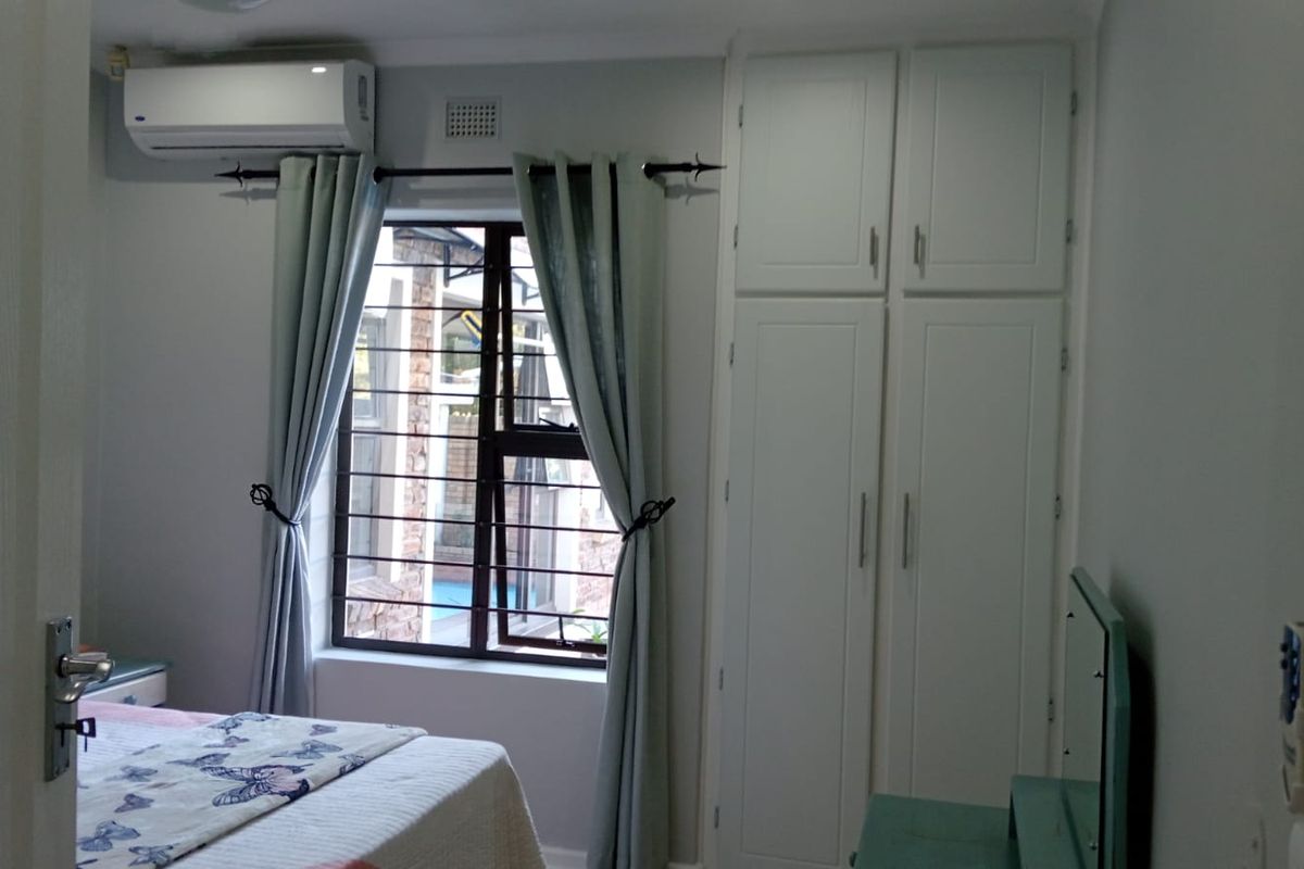 A bedroom featuring built-in cupboards, a window with security bars, and a wall-mounted air conditioning unit.