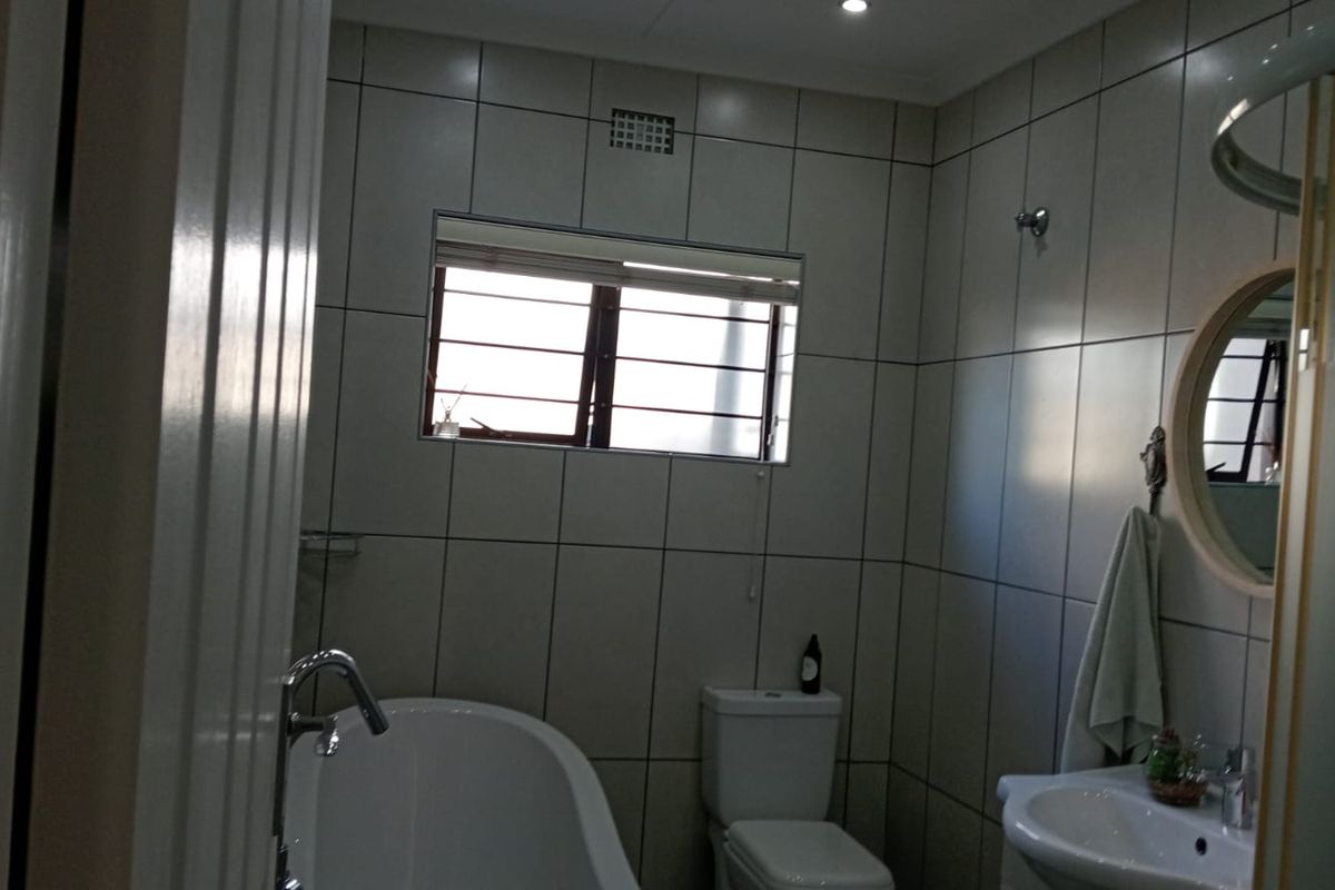 A functional bathroom featuring full-height wall tiling, a bathtub, a pedestal basin, and a toilet.