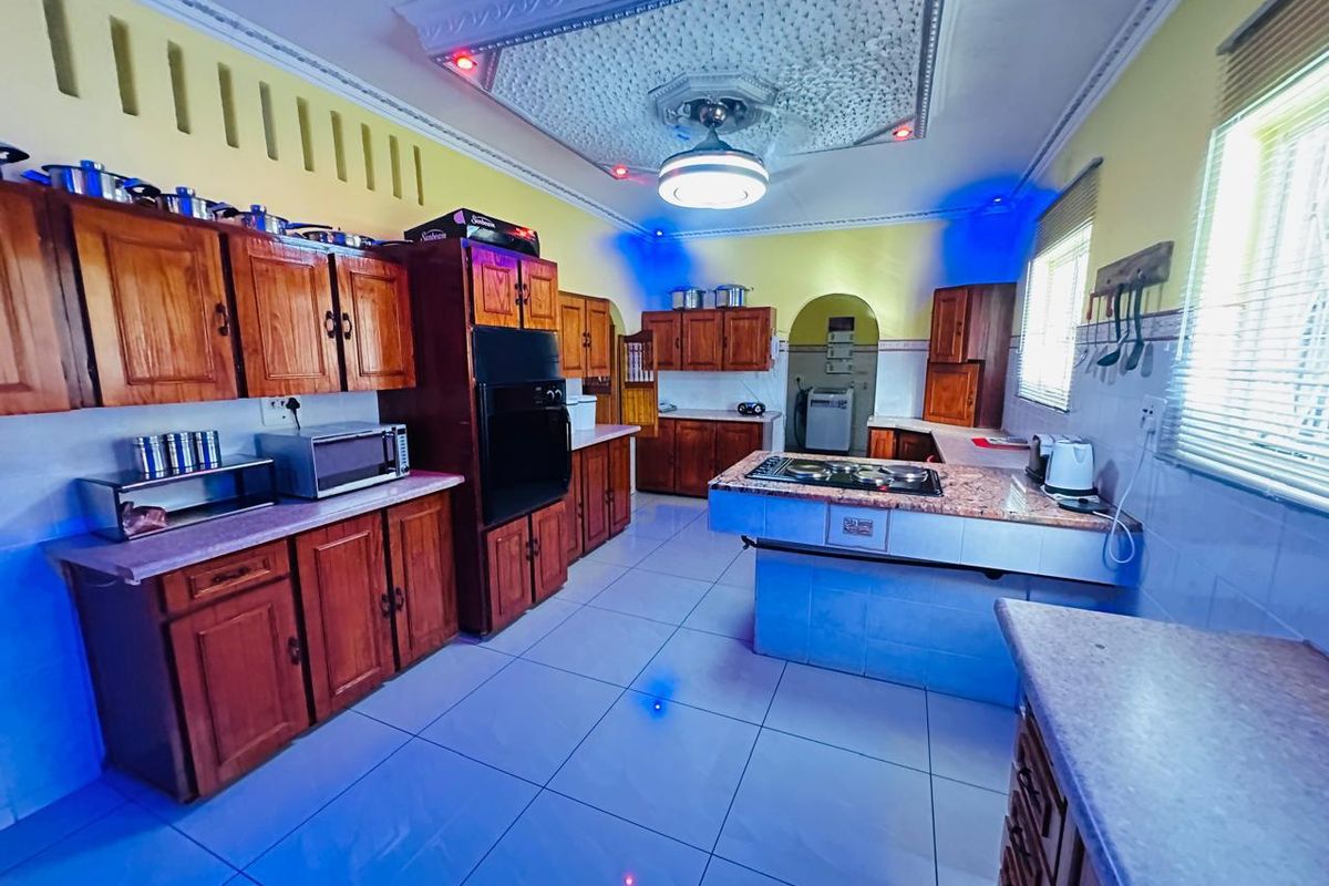 Spacious kitchen featuring extensive wooden cabinetry, a central island with integrated cooktop, tiled flooring, and decorative ceiling detailing.