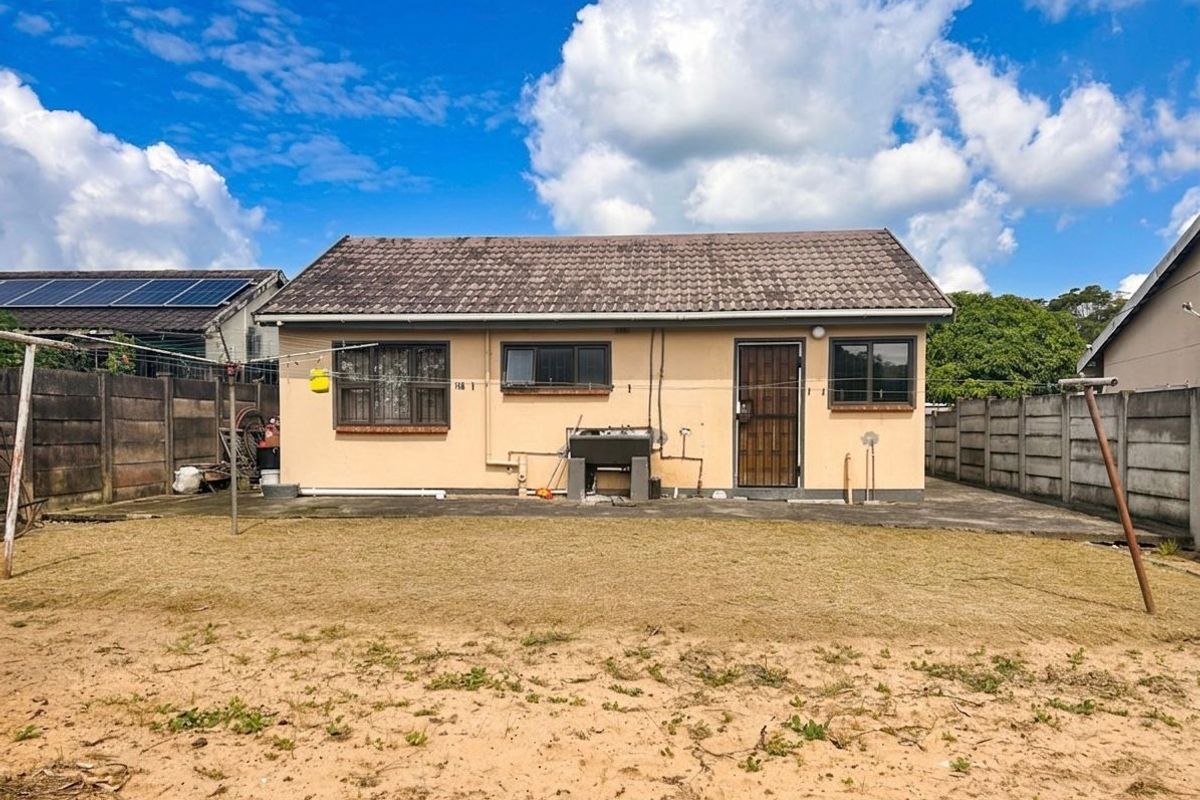 Rear view of a detached house featuring a tiled roof, concrete patio area, and a spacious backyard with perimeter walling.