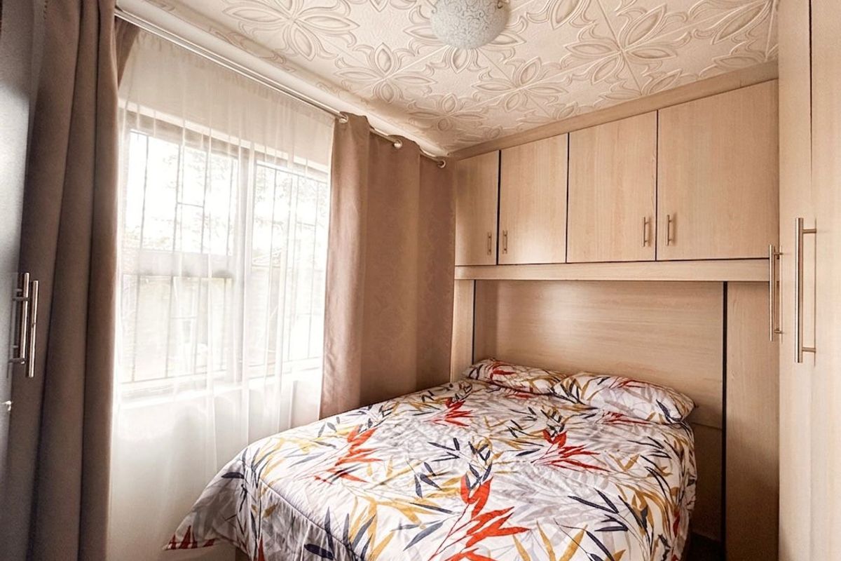 A compact bedroom featuring built-in light wood cabinetry and overhead storage, complemented by a decorative patterned ceiling and natural light from the window.