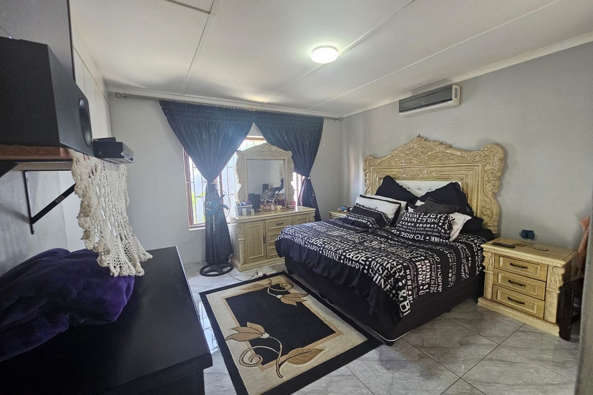 A spacious bedroom featuring tiled flooring, a wall-mounted air conditioning unit, and large windows with dark curtains.