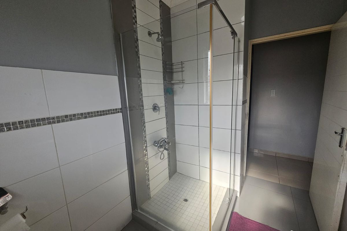 A functional bathroom featuring a glass-enclosed shower with white wall tiles, mosaic accent detailing, and tiled flooring.