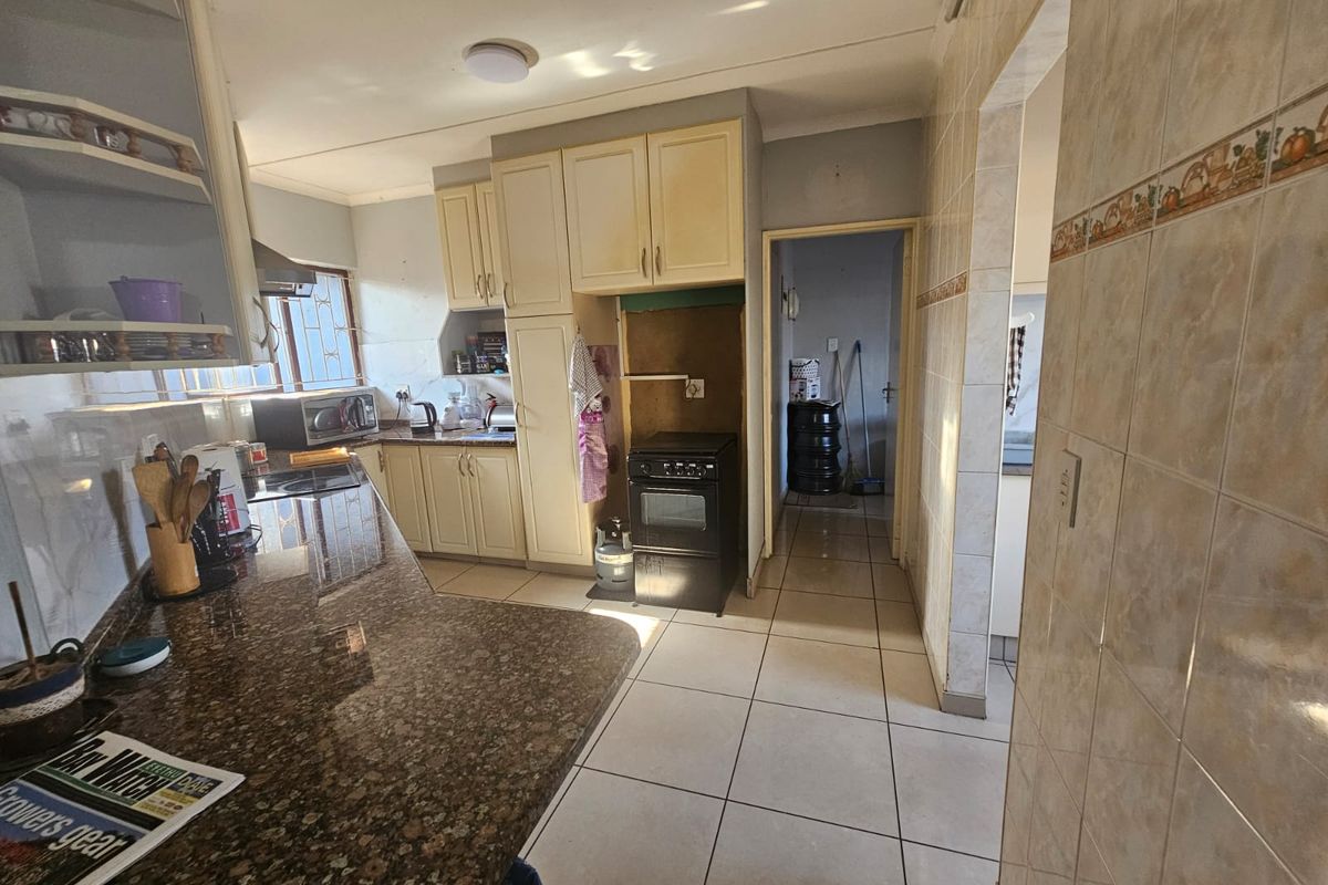 A functional kitchen featuring granite countertops, built-in cabinetry, and tiled flooring, with an adjacent utility area visible through the doorway.