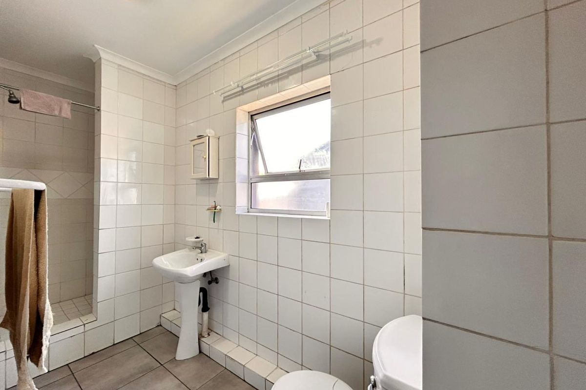 A functional bathroom featuring a pedestal basin, a walk-in shower with tiled surround, and a window for natural ventilation.