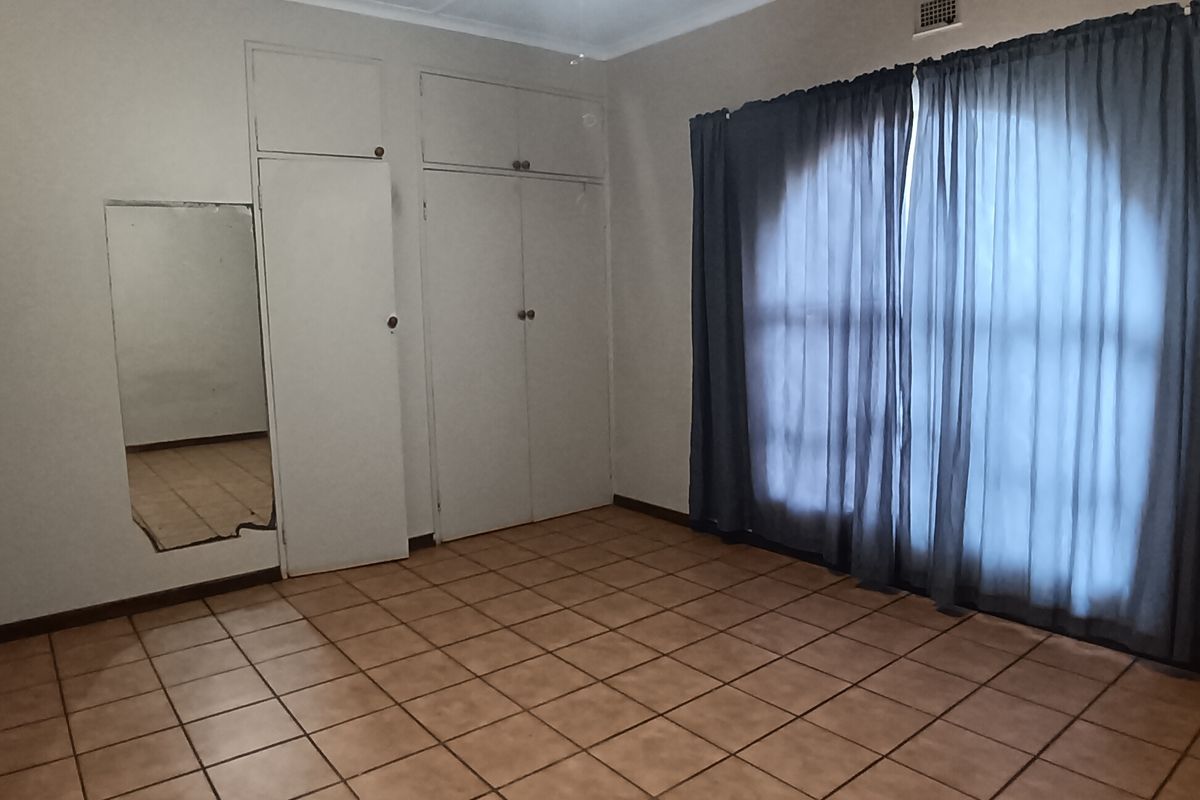 A spacious bedroom featuring built-in cupboards, tiled flooring, a ceiling fan, and large windows with curtains.