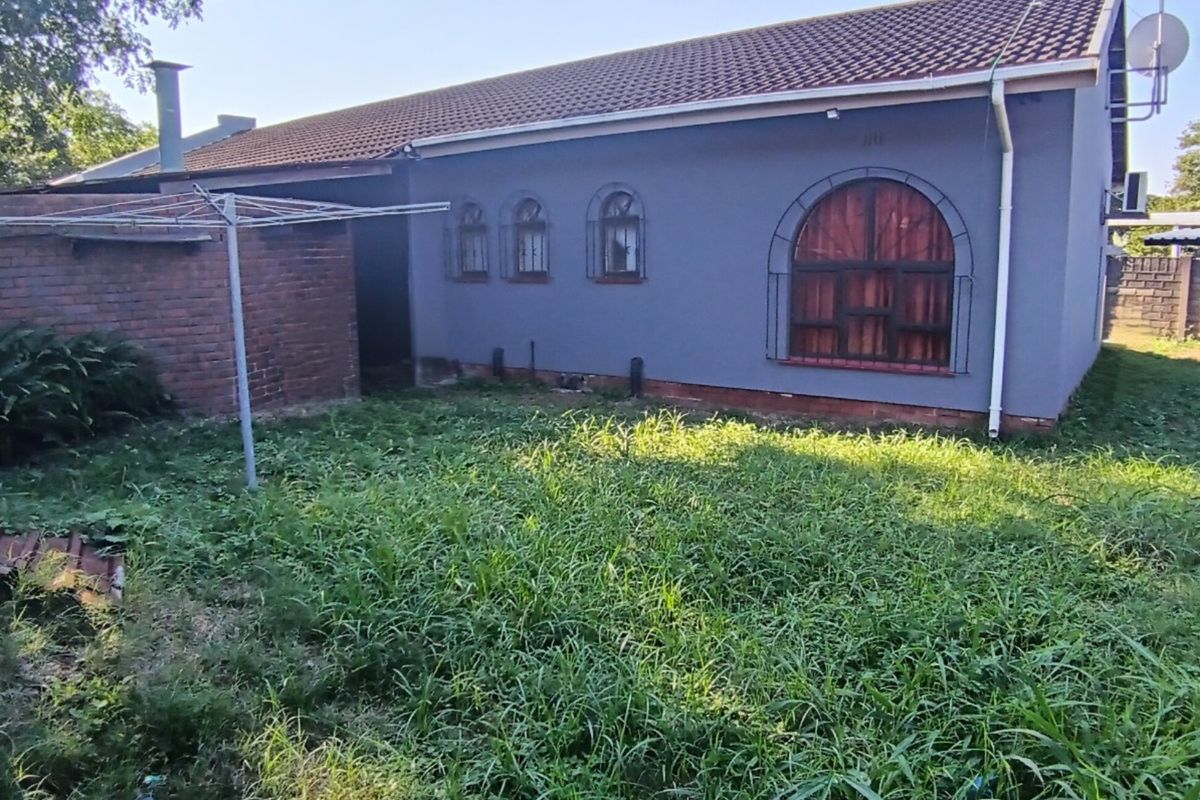 Rear view of the house featuring a tiled roof, arched windows with security bars, and an attached brick structure in the backyard.