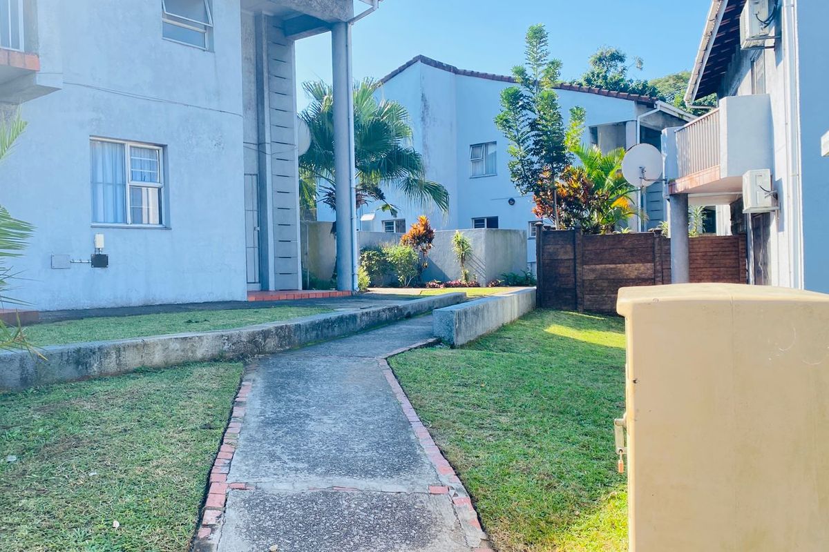 A view of the townhouse complex exterior featuring a concrete pathway leading through a shared garden area between residential units.