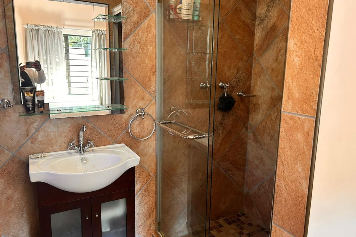 A functional bathroom featuring a glass-enclosed shower, a vanity basin with storage, and tiled wall finishes.
